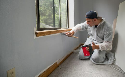 A Man Performing Residential Interior Painting On A Window In A Room.